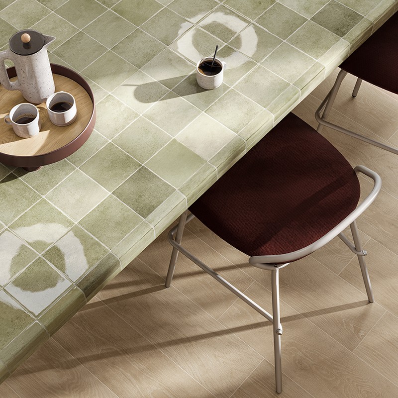 Grüne quadratische Fliesen-Tischplatte mit weißen Kreisflecken, Kaffeekanne und zwei Tassen auf Tablett, einzelne Kaffeetasse, Metallstuhl mit braunem Sitz, heller Holzfußboden.