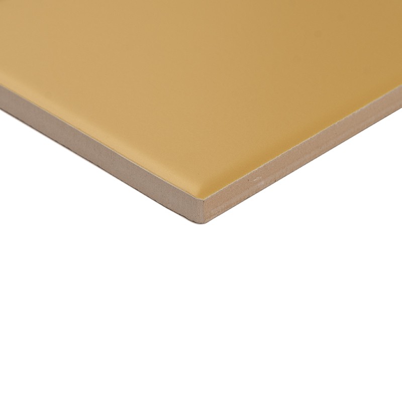 Mustard-colored tile with a smooth surface and soft gloss, exposed edge with ceramic core; isolated on a white background, showing a corner and the thickness of the material.