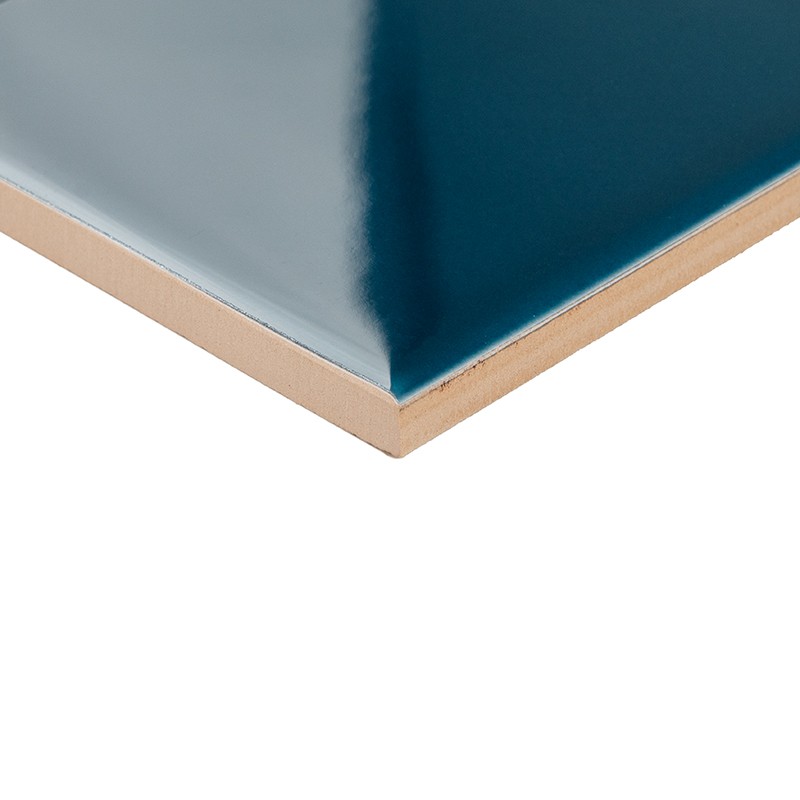 Blue ceramic tile with clay edge seen at an angle; shiny surface with reflection, beveled edge, on a white background.