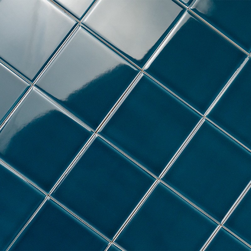 Carrelage composé de carreaux céramiques carrés bleu profond, joints fins clairs; gros plan en diagonale montrant surface brillante, reflets doux et dégradé bleu-vert.