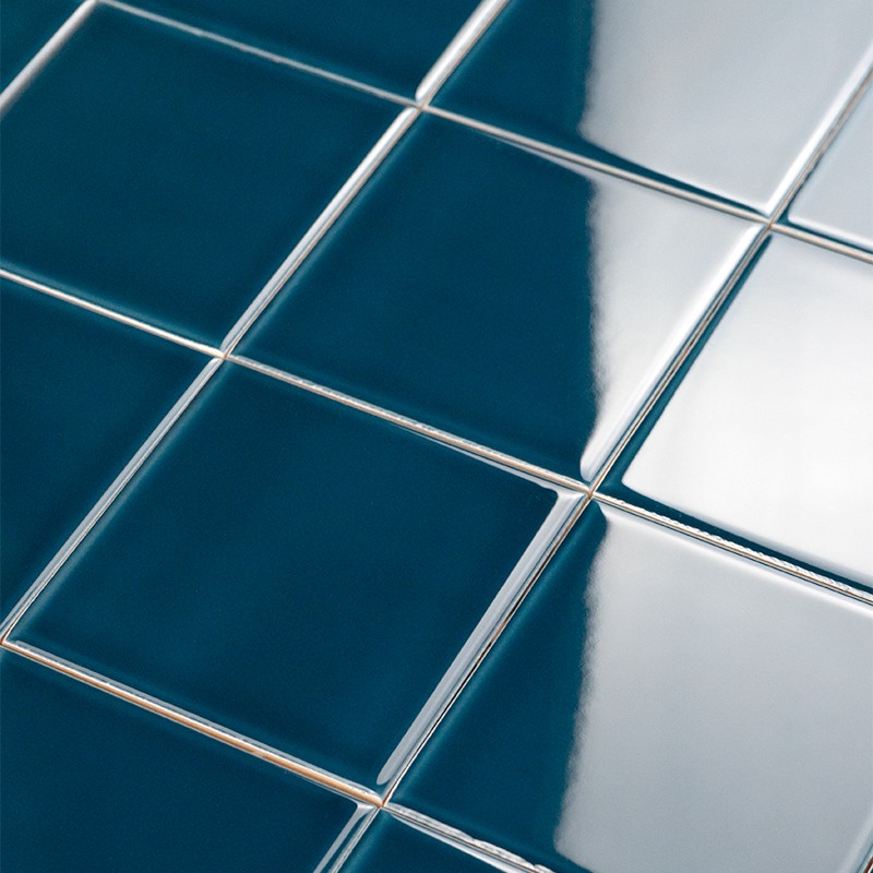 Carrelage carré émaillé bleu profond, joints fins blancs; surfaces très réfléchissantes montrant un large reflet lumineux vertical et une transition de teinte plus claire à droite.