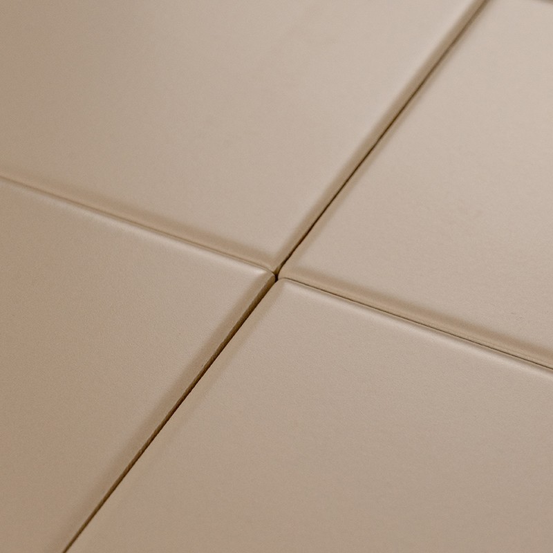 Azulejo beige mate con bordes biselados y juntas estrechas formando una cruz; contexto: unión de cuatro baldosas sobre una superficie continua.