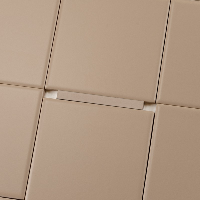Azulejo cuadrado beige liso en primer plano; juntas visibles con separador blanco entre bordes, rodeado por azulejos cuadrados similares en patrón alineado.