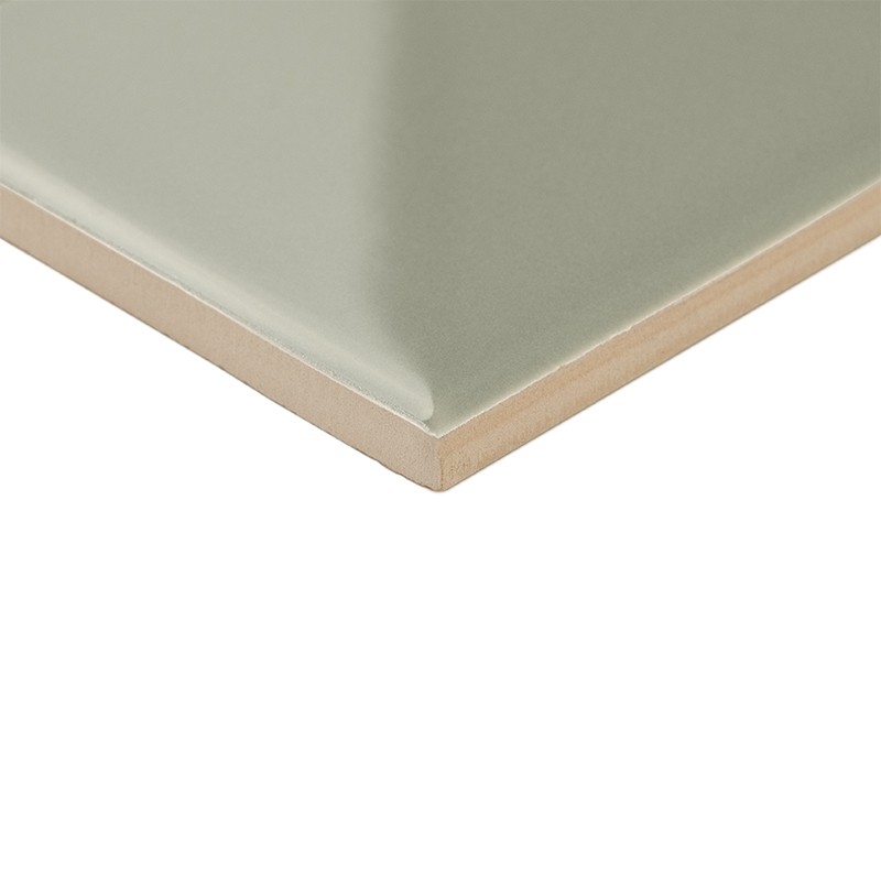 Azulejo cuadrado verde grisáceo esmaltado brillante visto en esquina; núcleo beige visible en canto biselado; sobre fondo blanco neutro.
