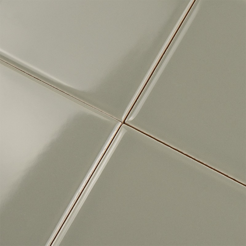 Square ceramic tile, pale green and glossy; narrow joints forming a central cross, reflective surface and clean outline on a wall covering.
