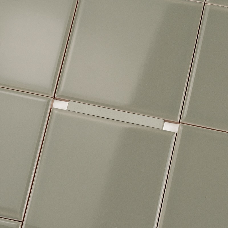 Plain greyish-green square tile; joints with beige grout and white spacers, surrounded by identical tiles in a lattice pattern.