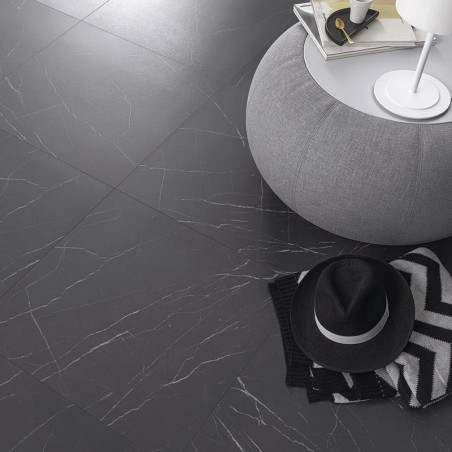Um piso de cerâmica cinza escuro com padrão de mármore sustenta uma poltrona cinza com livros e uma luminária. Um chapéu preto e Um piso de cerâmica cinza escuro com padrão de mármore sustenta uma poltrona cinza com livros e uma luminária. Um chapéu preto e