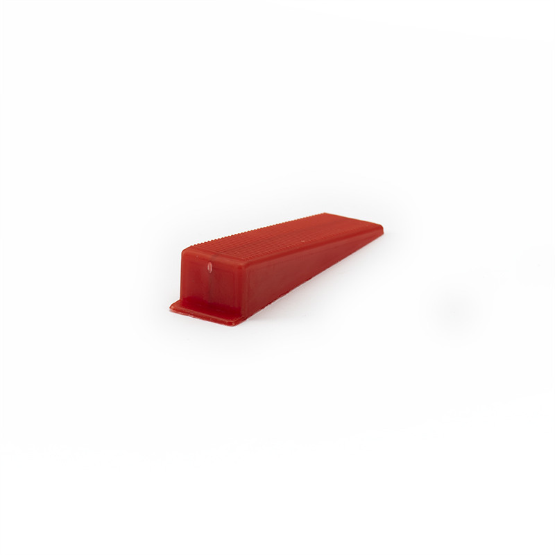 Un tope de puerta rojo en forma de cuña se encuentra sobre una superficie blanca lisa, ligeramente inclinado hacia arriba, sin t