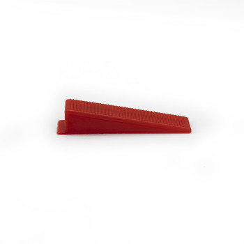 Ein roter Plastikkeil ruht auf einer schlichten weißen Oberfläche. Die schräge Seite weist eine gerippte Struktur auf.