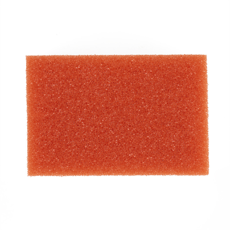 Une éponge rectangulaire orange repose sur un fond blanc uni, présentant une surface texturée et poreuse.