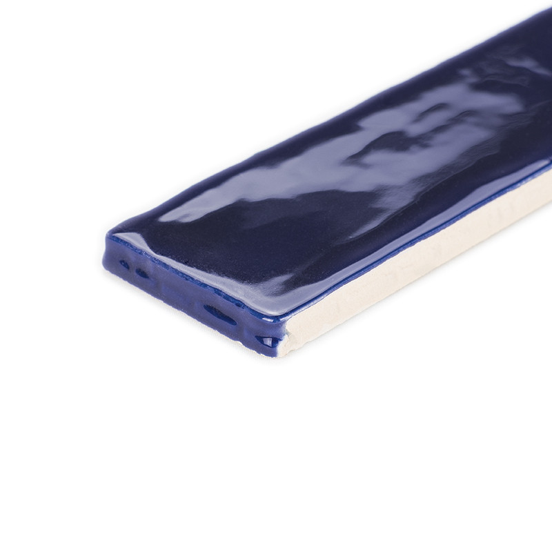 Um ladrilho retangular revestido com esmalte azul escuro brilhante repousa sobre uma superfície branca, exibindo seu acabamento 