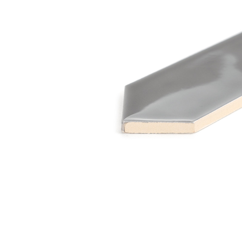 A gray, glossy tile positioned on a white surface, cut to reveal its cream-colored interior, with a hexagonal edge on display.