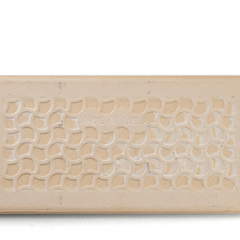 Eine rechteckige beige Fliese zeigt ein sich wiederholendes Muster aus ineinandergreifenden Halbkreisen. In der Mitte steht in s