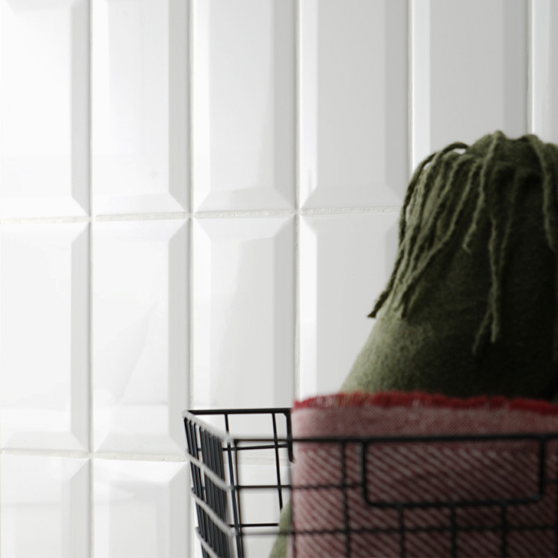 A black wire basket holds green and red folded blankets on a glossy, white tiled surface with a geometric pattern.