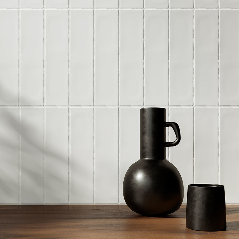 A matte black vase and cup rest on a wooden surface, set against a white tiled wall casting soft shadows.