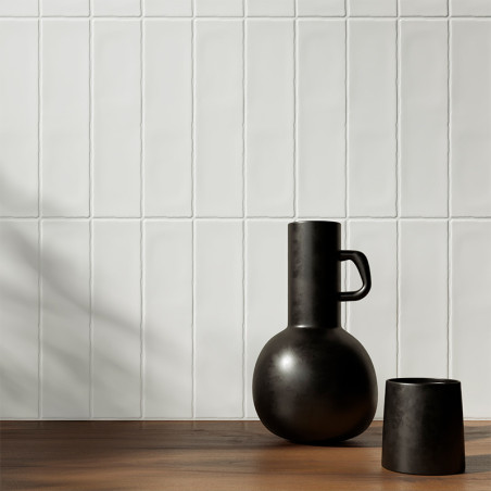 A matte black vase and cup rest on a wooden surface, set against a white tiled wall casting soft shadows. A matte black vase and cup rest on a wooden surface, set against a white tiled wall casting soft shadows.