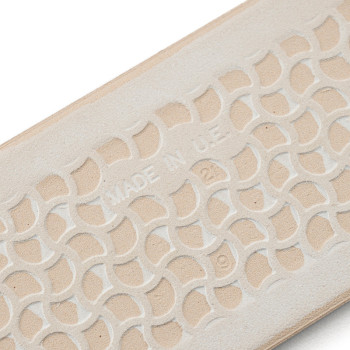 Eine beige Gummisohle weist ein erhabenes, ineinandergreifendes geometrisches Muster mit dem Text „MADE IN U.S.A.“ auf. in der M