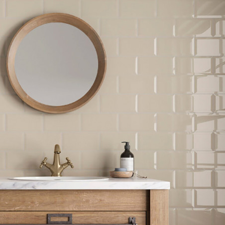 Über einer beige gefliesten Wand hängt ein runder Spiegel. Der Waschtisch aus Holz trägt ein Marmorwaschbecken mit Messinghahn u