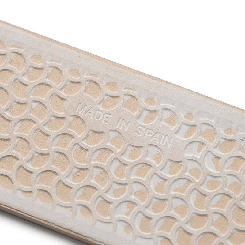 Superficie con textura beige con semicírculos superpuestos en relieve que muestran `MADE IN SPAIN`, lo que sugiere artesanía en 