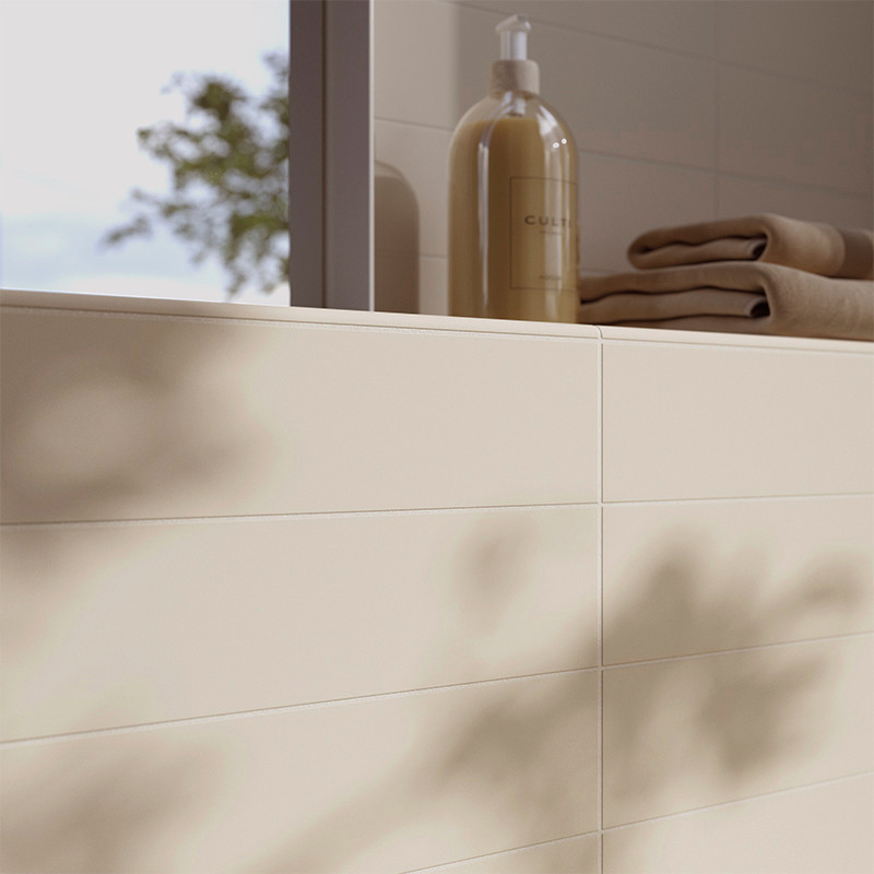 Cremefarbene Fliesen säumen die Wand eines Badezimmers und werfen sanfte Schatten. Daneben stehen auf einem Sims ein Seifenspend
