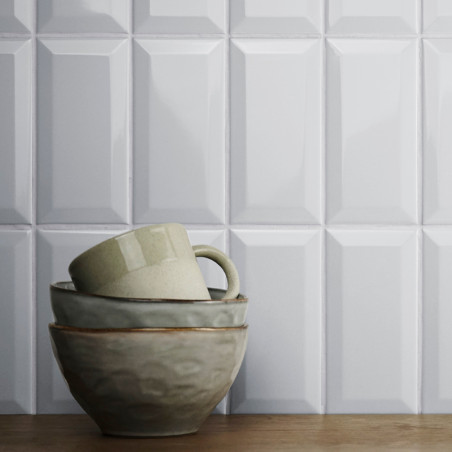Ein Stapel Keramikschalen und ein Becher stehen auf einer Holzoberfläche vor glänzenden, geometrisch gemusterten weißen Wandflie Ein Stapel Keramikschalen und ein Becher stehen auf einer Holzoberfläche vor glänzenden, geometrisch gemusterten weißen Wandflie