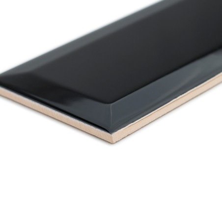 Eine glänzend schwarze rechteckige Fliese mit abgeschrägten Kanten liegt schräg und präsentiert ihre glatte Oberfläche im Kontra