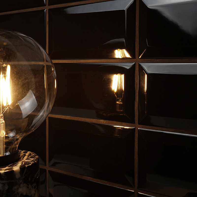 Een gloeiende gloeilamp straalt warm licht uit, gereflecteerd op glanzend zwarte, rechthoekige tegels. De opstelling zorgt voor 