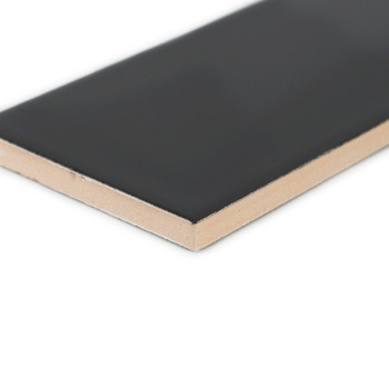 A rectangular ceramic tile, featuring a smooth black surface and a beige underside, rests on a plain white background.