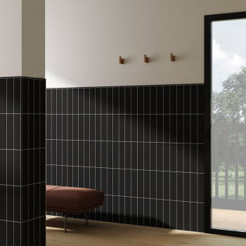 Black vertically striped tiles cover walls. a brown bench stands against them. A glass door opens to a lush green view.