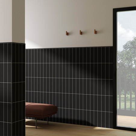 Black vertically striped tiles cover walls. a brown bench stands against them. A glass door opens to a lush green view.