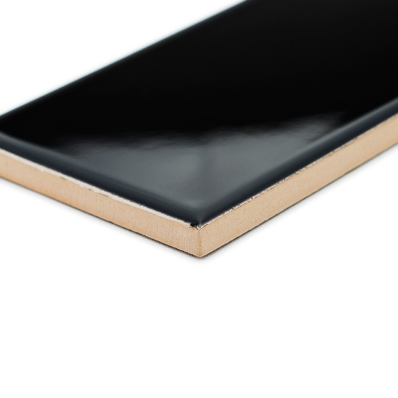 Un carreau de céramique noir brillant présente son bord angulaire exposé, mettant en valeur sa surface lisse sur un fond blanc u