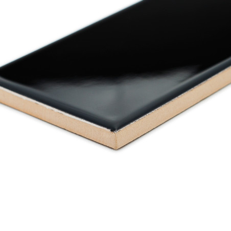 Un carreau de céramique noir brillant présente son bord angulaire exposé, mettant en valeur sa surface lisse sur un fond blanc u