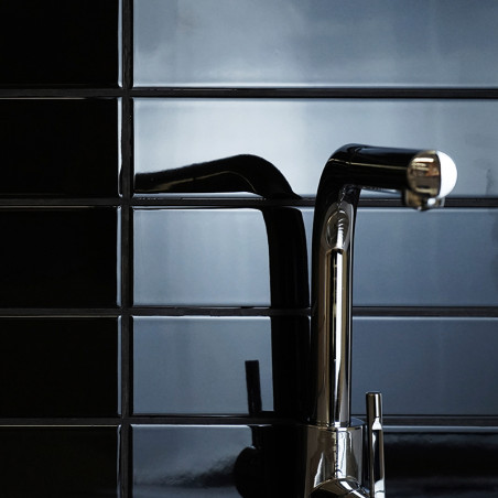 Un élégant robinet chromé s'étend horizontalement, réfléchissant la lumière sur un mur carrelé noir brillant, créant ainsi un dé