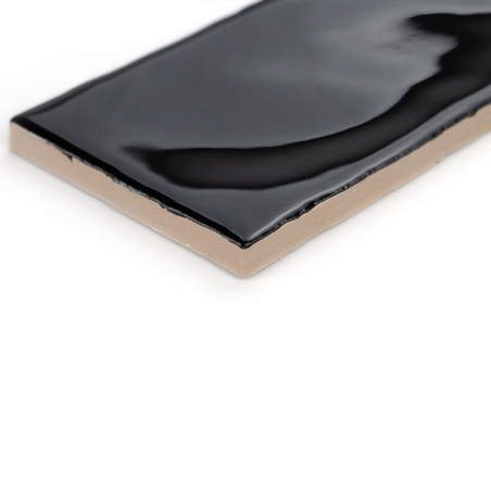 Eine rechteckige Keramikfliese weist eine glänzend schwarze Oberfläche mit leichten Wellen vor einem neutralen weißen Hintergrun Eine rechteckige Keramikfliese weist eine glänzend schwarze Oberfläche mit leichten Wellen vor einem neutralen weißen Hintergrun