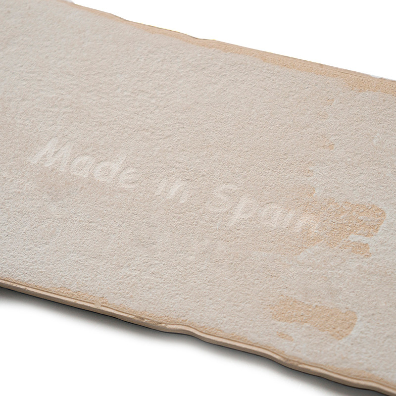 Azulejo rectangular de color blanquecino con superficie texturizada. El texto `Made in Spain` está sutilmente grabado en el cent