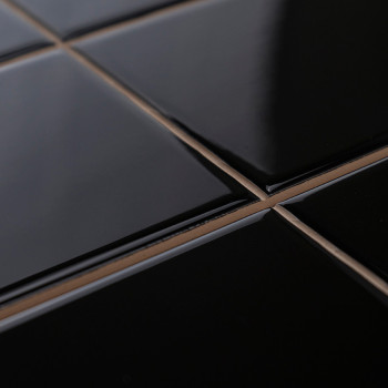 Carreaux noirs brillants disposés selon un motif en grille, réfléchissant la lumière, avec un coulis de couleur beige, créant un