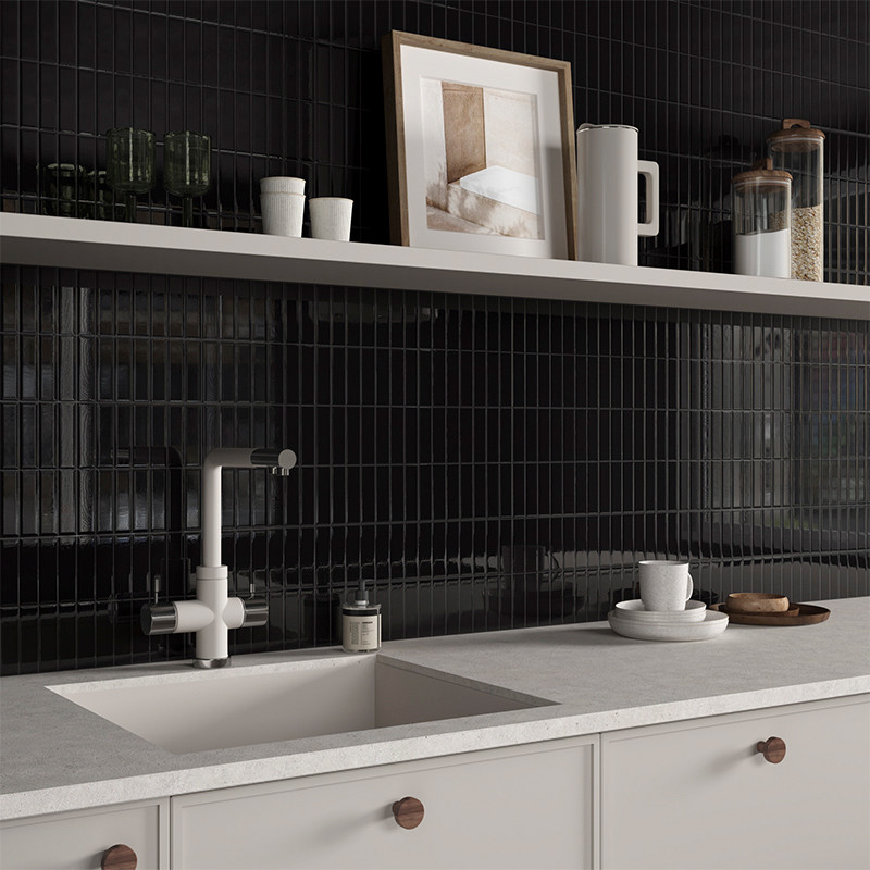 A minimalist kitchen countertop features a modern faucet and sink, set against a backdrop of glossy black tile with open shelvin