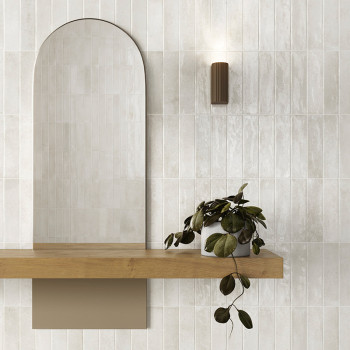 Een gebogen spiegel rust boven een houten plank, vergezeld van een weelderige, hangende plant. Een moderne, cilindrische wandkan