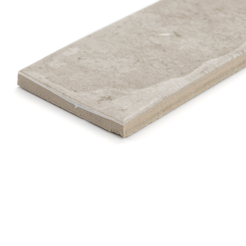 Un carreau de céramique rectangulaire beige repose sur un fond blanc. Le carreau a une finition mate avec de subtiles variations