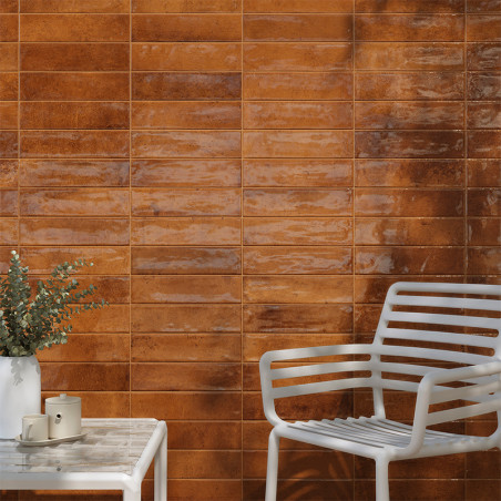 Eine Wand aus glänzenden, braunen rechteckigen Fliesen reflektiert das Licht und befindet sich hinter einem Stuhl und Tisch aus 