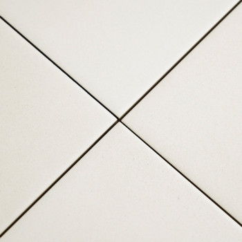 Vier witte keramische tegels ontmoeten elkaar op een centraal punt en vormen een plusvorm met smalle voeglijnen, geplaatst in ee