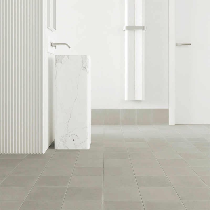 Square tiles cover a minimalist bathroom floor, featuring a sleek, marble pedestal sink with a modern faucet, against a white wa