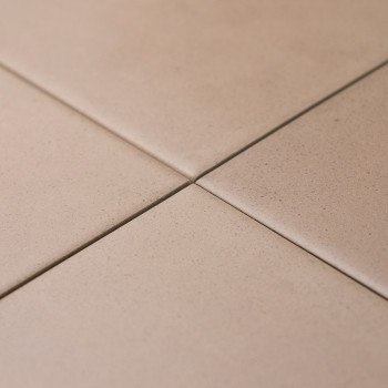 Vier beige Fliesen kreuzen sich sauber und bilden an ihren Ecken ein kleines Kreuz. Sie sind auf einer flachen, ebenen Oberfläch