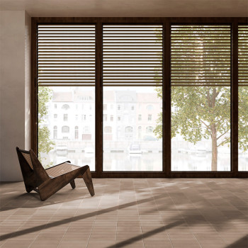 Una silla de madera se reclina sobre un suelo de azulejos, frente a grandes ventanales con persianas abiertas, que revelan árbol