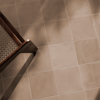 Ein Holzstuhl wirft seinen Schatten auf hellbraune, quadratische Keramikfliesen und schafft so eine warme und ruhige Atmosphäre 