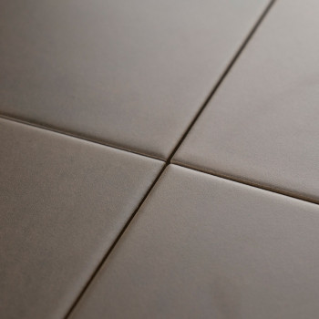 Vier glatte, matte, quadratische Fliesen treffen an einer zentralen Fugenlinie aufeinander und bilden ein minimales Gittermuster