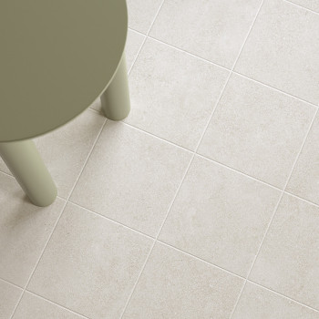 Un pied de table rond vert olive repose sur une grille de carreaux beige clair, créant un aspect de sol moderne et minimaliste.