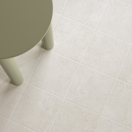Een ronde, olijfgroene tafelpoot staat op een raster van lichtbeige tegels, waardoor een moderne, minimalistische vloeruitstrali