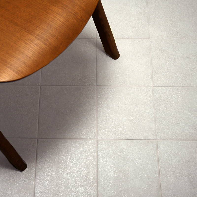 Una mesa redonda de madera cubre parcialmente una cuadrícula de azulejos de color gris claro, creando un ambiente interior cálid