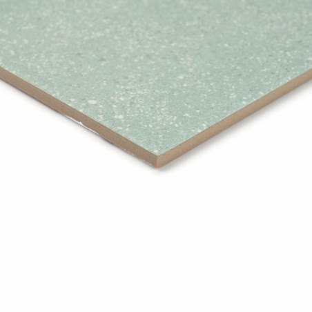 Um ladrilho cerâmico salpicado de verde assenta sobre um fundo branco, mostrando sua superfície lisa e polida e bordas angulares Um ladrilho cerâmico salpicado de verde assenta sobre um fundo branco, mostrando sua superfície lisa e polida e bordas angulares